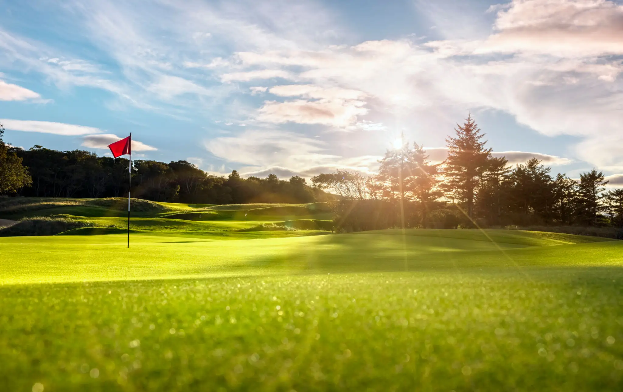 A sunlit golf course with a flagstick marking the hole.