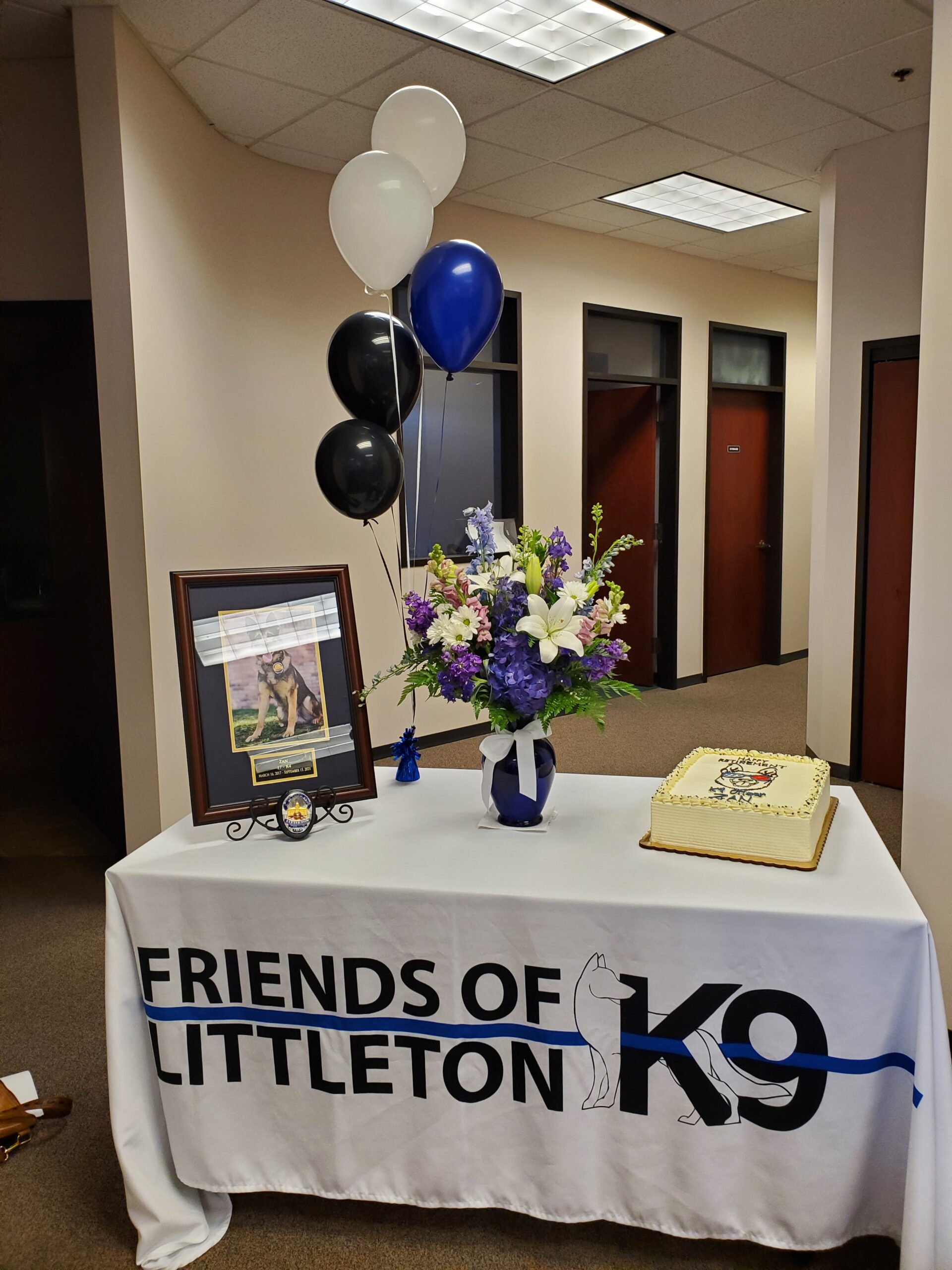 A decorated table for Friends of Littleton K9 with flowers, balloons, and a photo.