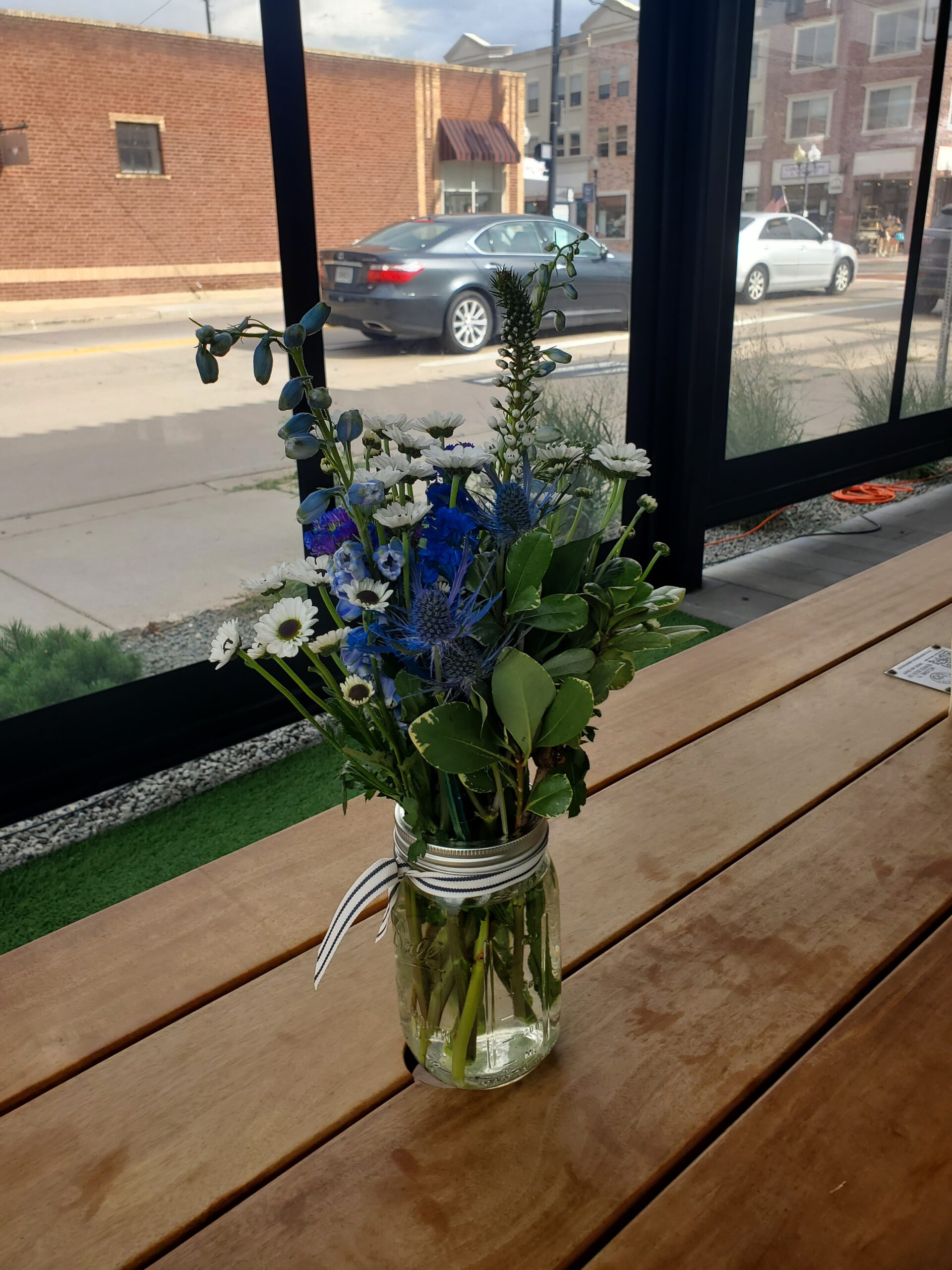 A glass jar with a bouquet of mixed flowers on a wooden table indoors.