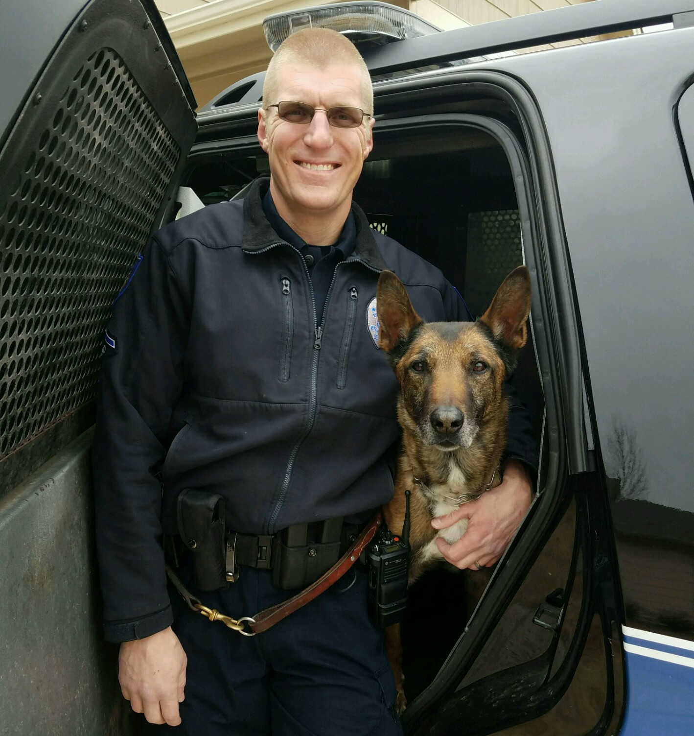 Police officer standing next to a police dog by a vehicle.