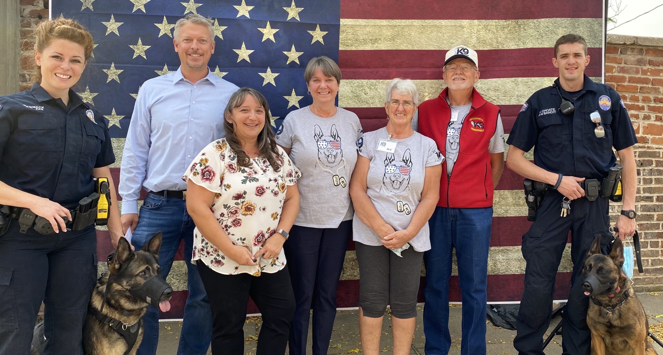 Group of five adults smiling in front of an American flag backdrop.
