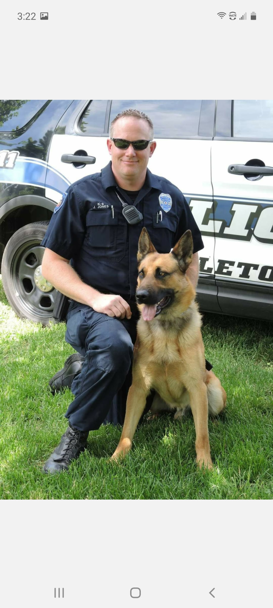 Police officer kneels beside a German Shepherd police dog outdoors.