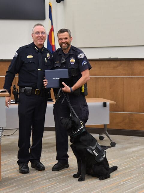 Two police officers and a police dog during an award ceremony indoors.