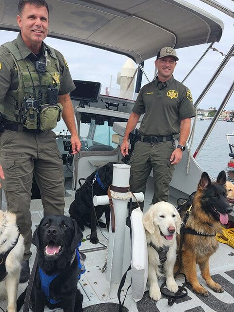 Three law enforcement officers with three service dogs on a boat.